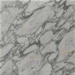 A close-up photograph of a polished Arabescato marble slab, featuring a soft white background showing dramatic, brecciated veining in varying tones of deep charcoal and soft grey.