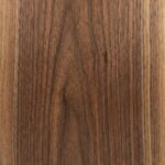 A close-up view of a polished American Walnut surface, displaying a rich, chocolate-brown background with consistent, straight grain lines and subtle hints of warm amber.