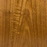 A close-up of a polished Gold Eucalyptus veneer, displaying a rippled, iridescent grain pattern in varying shades of honey, amber, and golden-brown.