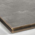 A close-up view of a Patina Bronze metal surface, showcasing a dark, warm brownish-bronze tone with subtle variations in color and a soft, hand-rubbed satin sheen.