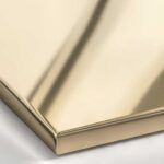 A macro shot of a Polished Bronze metal surface, displaying a highly reflective, golden-brown mirror finish with warm amber undertones.